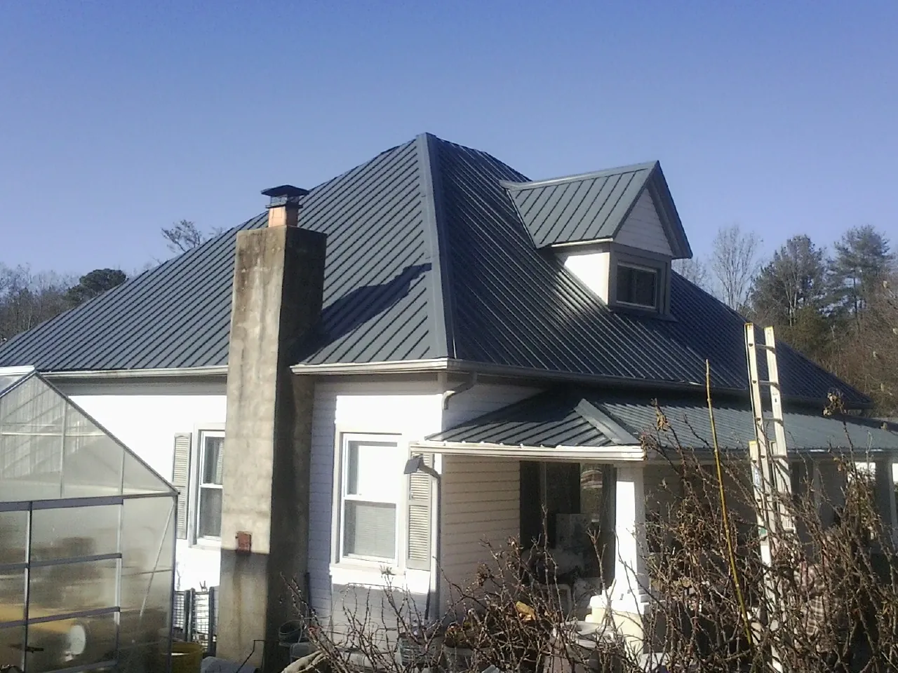 Dark blue standing seam metal roof on a white farmhouse with dormer — Slate & Tile Roof Repair by Roofing Brothers in Lamona