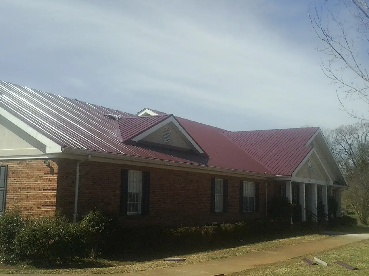Red metal roof with gabled entries on a long brick building, from a Hail Damage Roof Repair job in Lamona