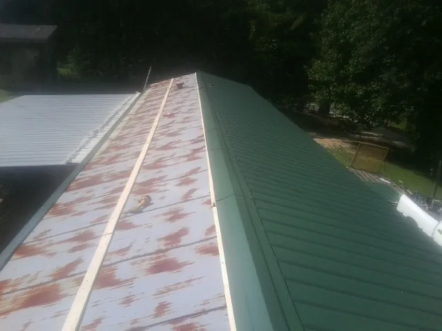 Old rusted panels beside newly installed green metal roofing — Wind Damage Roof Repair by Roofing Brothers in Lamona
