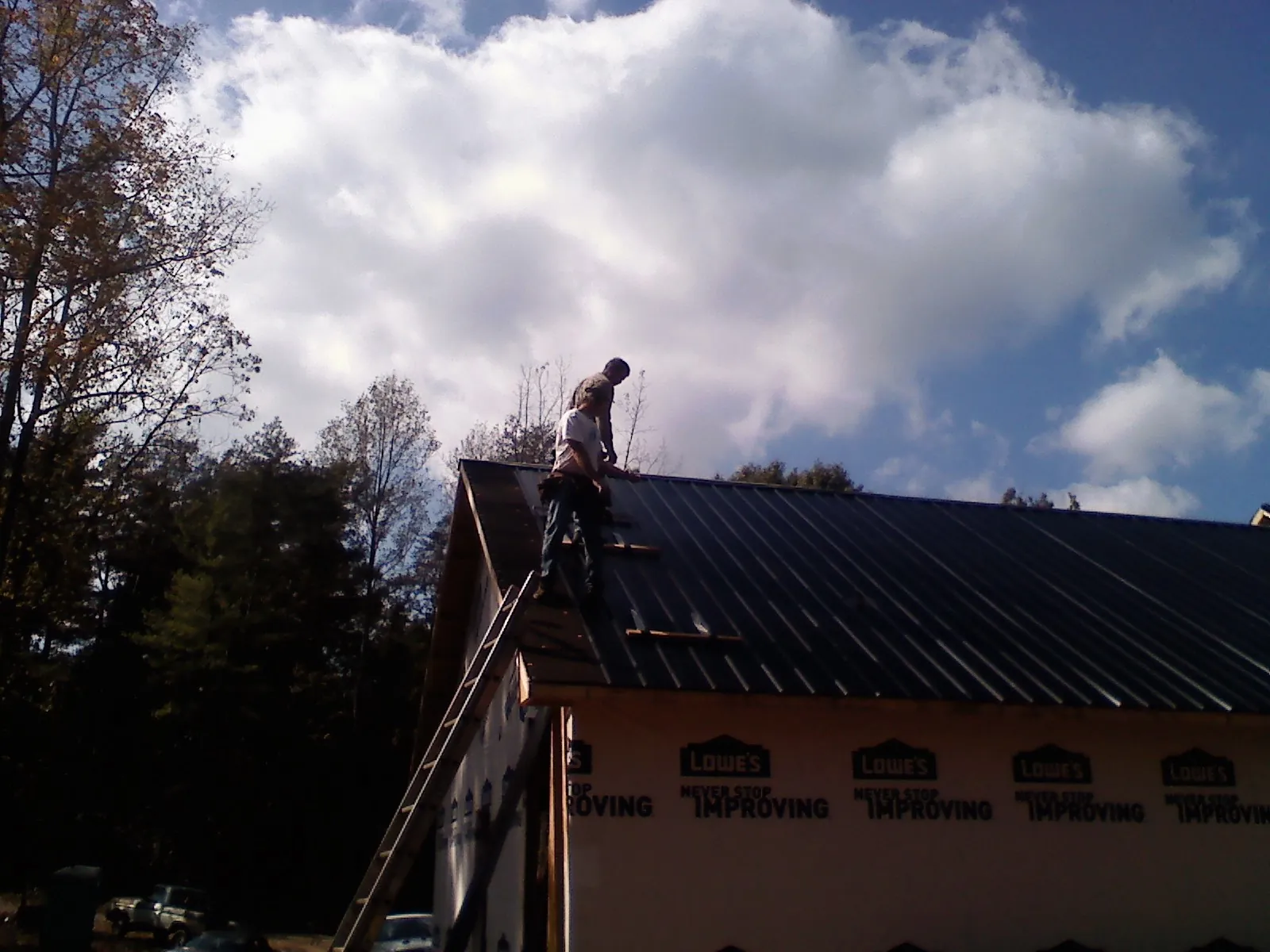 Roofer fastening dark metal panels high against a cloudy sky, from a Roof Inspection job in Lamona