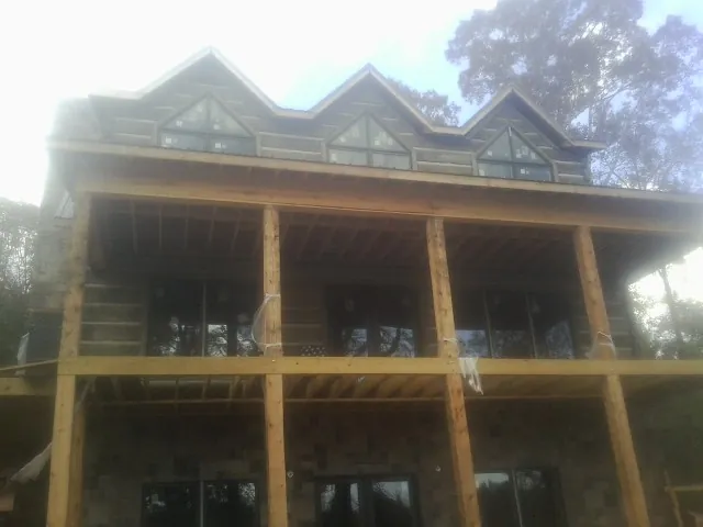 Dormers and porch framing on a large log home under construction — Roof Coating work by our crew in Lamona