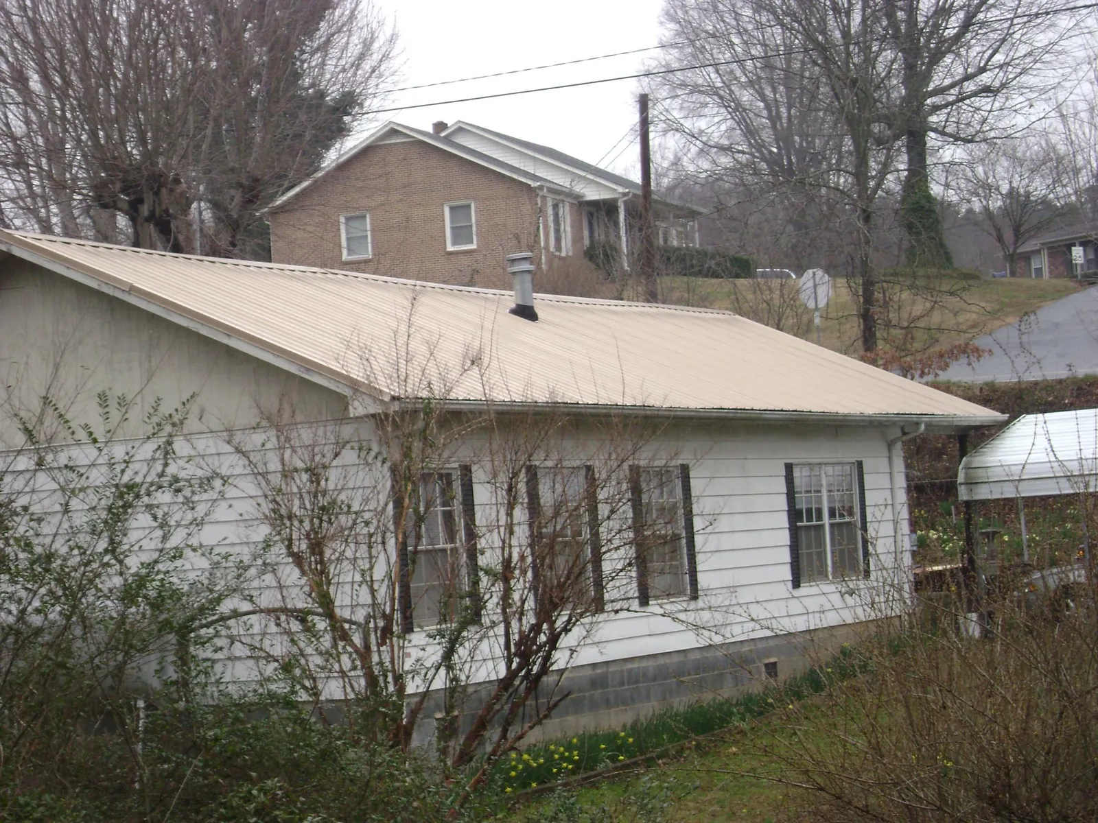 Tan metal roof on a white sided house set into a hillside — Commercial Roofing by Roofing Brothers in Lamona