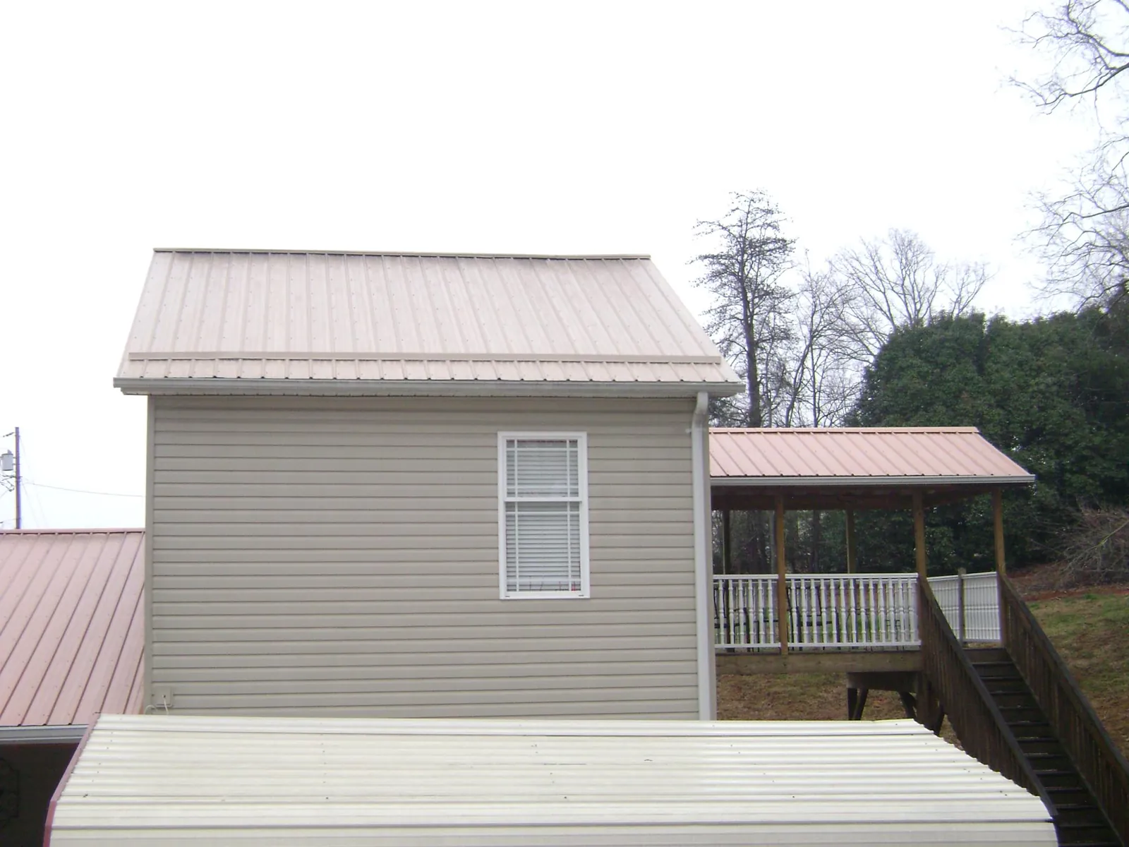 Tan metal roofs on a two story addition and attached porch, from a Roof Replacement job in Lamona